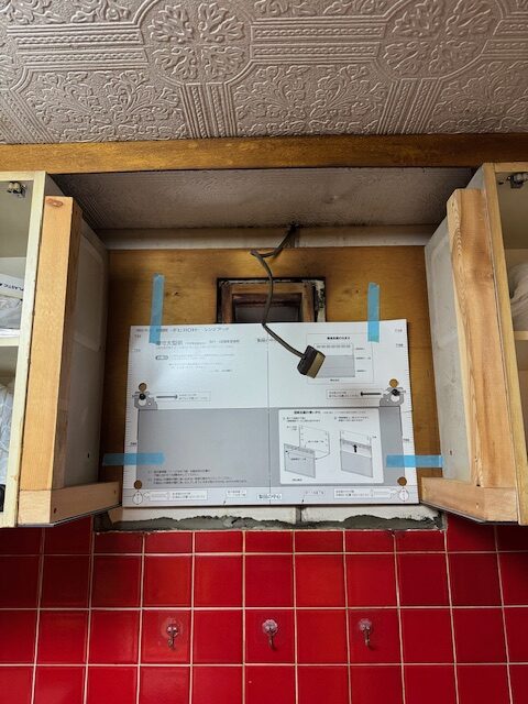 左右の吊戸棚に木材を取り付けて隙間を造作加工します。型紙が貼ってありますが、この型紙のサイズのまま新しいレンジフードが設置されます。